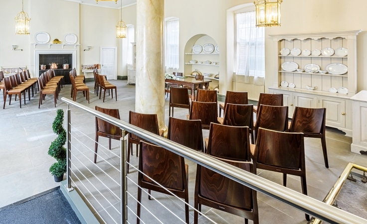 A room with chairs, a column, a tiled floor and cabinets that have ornamental plates in them.